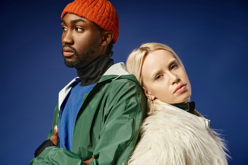 young blonde woman leaning on african american man in winter attire, diverse models on blue backdrop